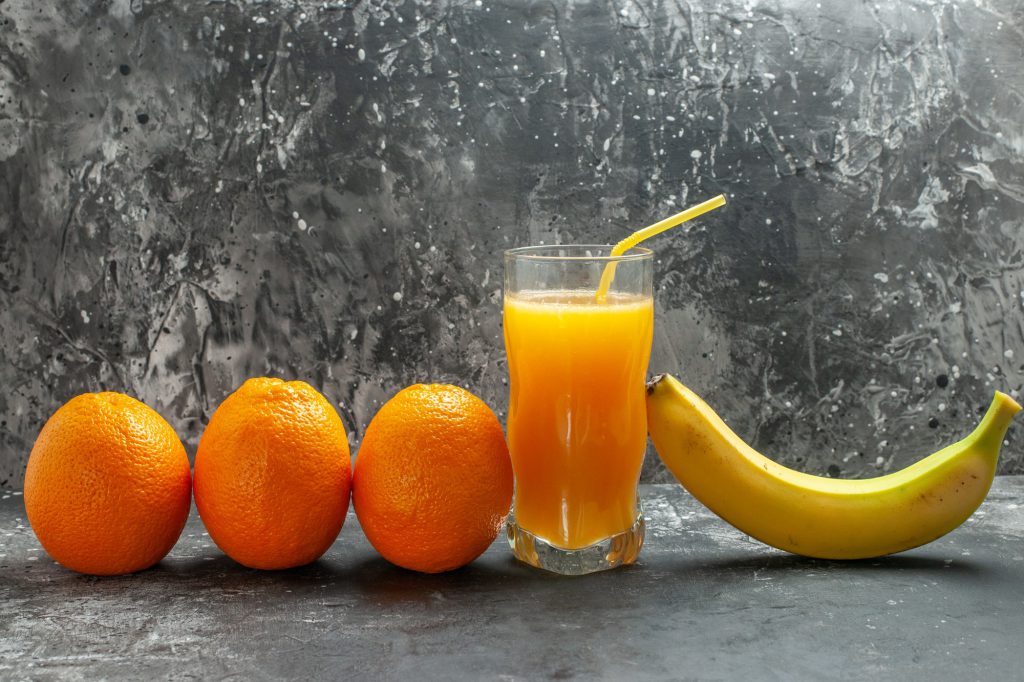 Top view of vitamin source fresh oranges banana and juice on gray background